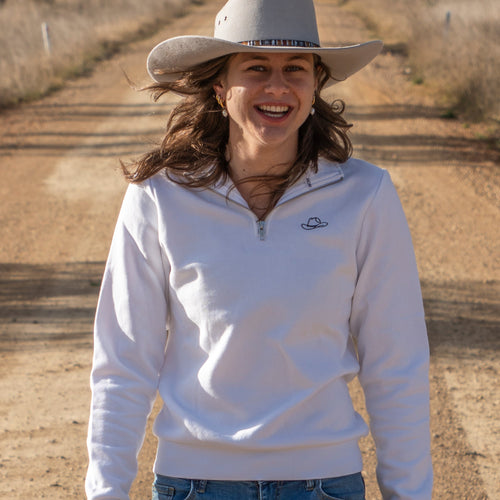 Woman wearing a white sweatshirt and cowboy hat on a dirt road with trees in the background