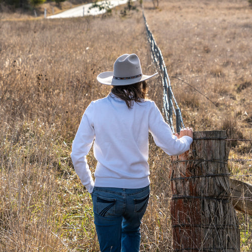 Person walking along a wooden fence in a rural landscape with trees and open fields.