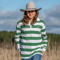 Person wearing a green and white striped shirt and cowboy hat in a field with trees and blue sky in the background