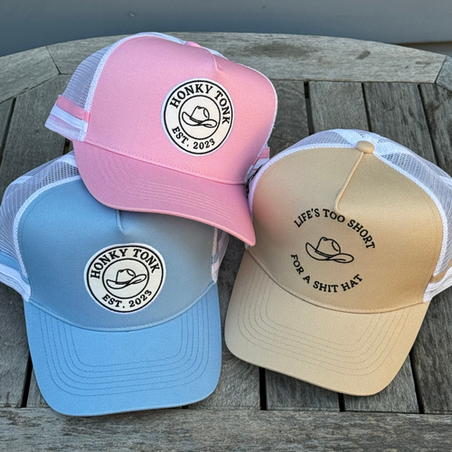 Three caps in pink, blue, and beige on a wooden surface with text and logos.