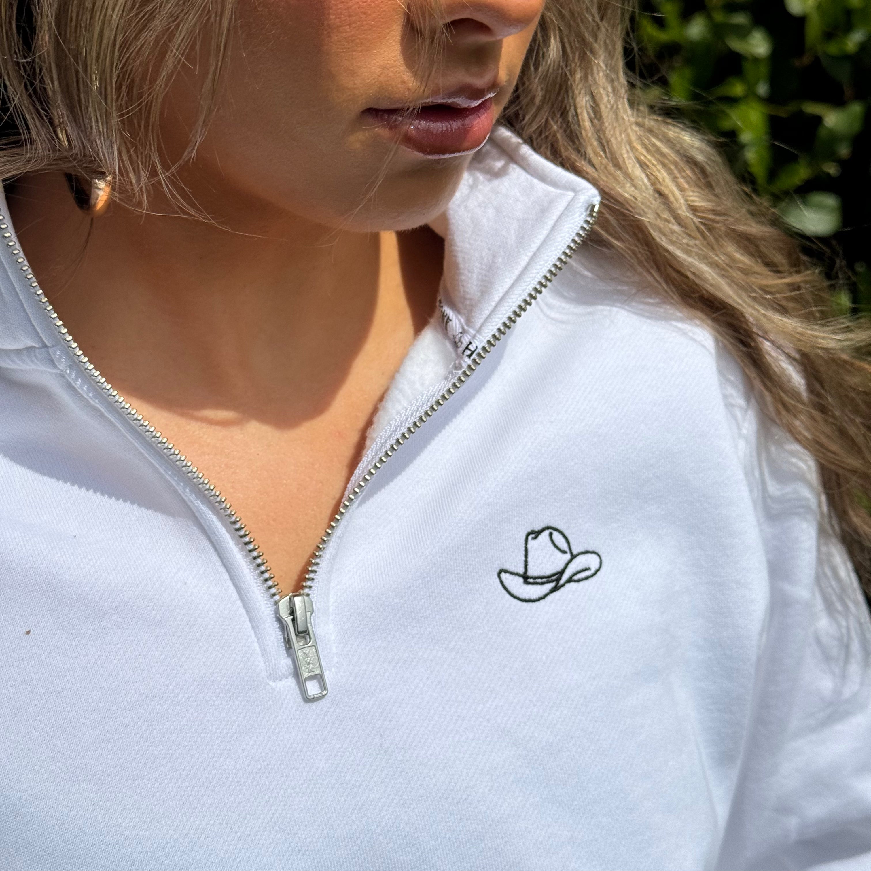 White zip-up sweatshirt with a small embroidered design on a person outdoors.