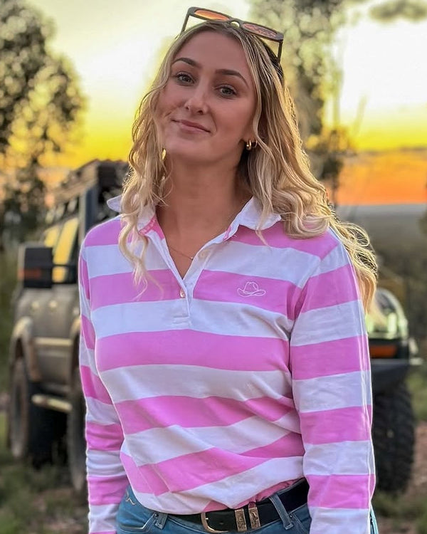 Woman in a pink and white striped shirt standing outdoors with a sunset in the background